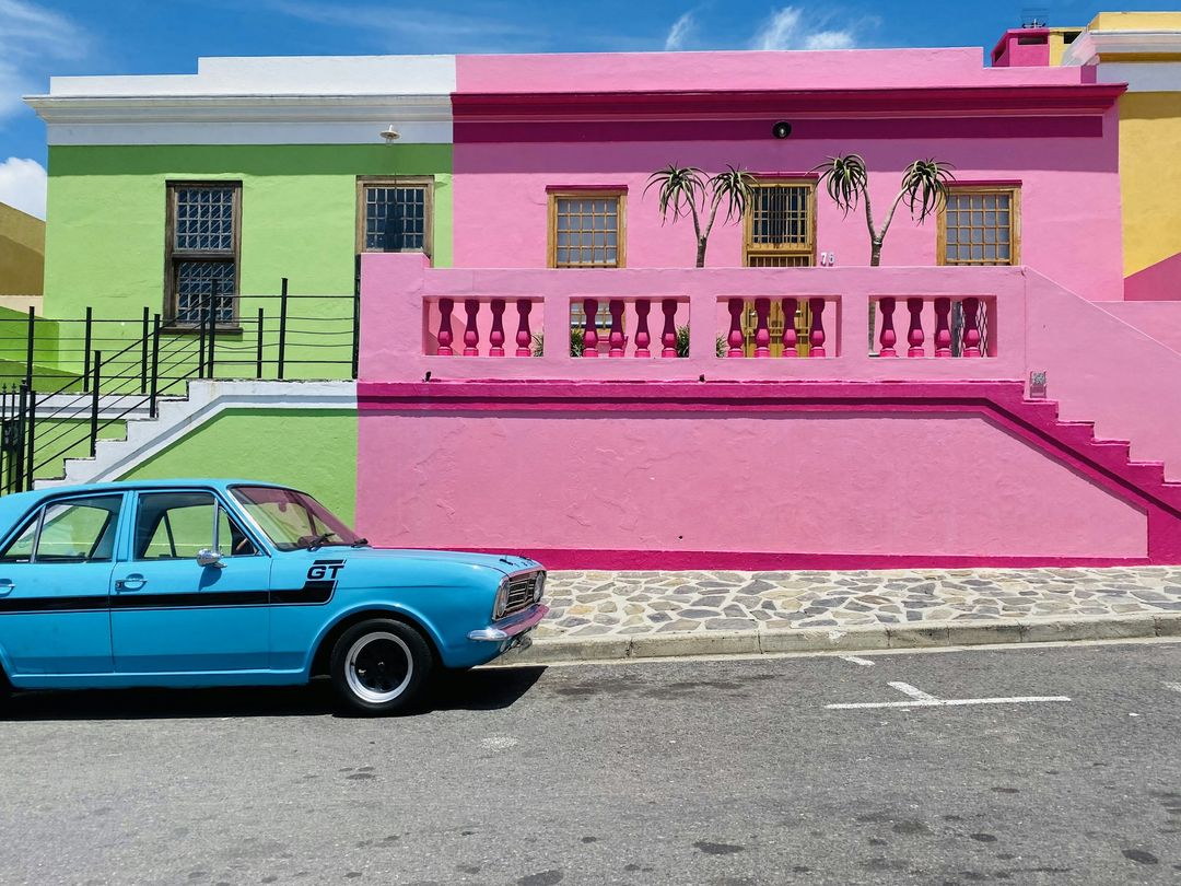 A lime-green house beside a pink one, a pale blue vintage car parked in front