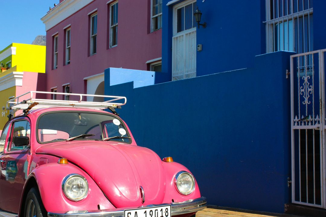A pink Volkswagen Beetle in front of a deep blue house and a pink one