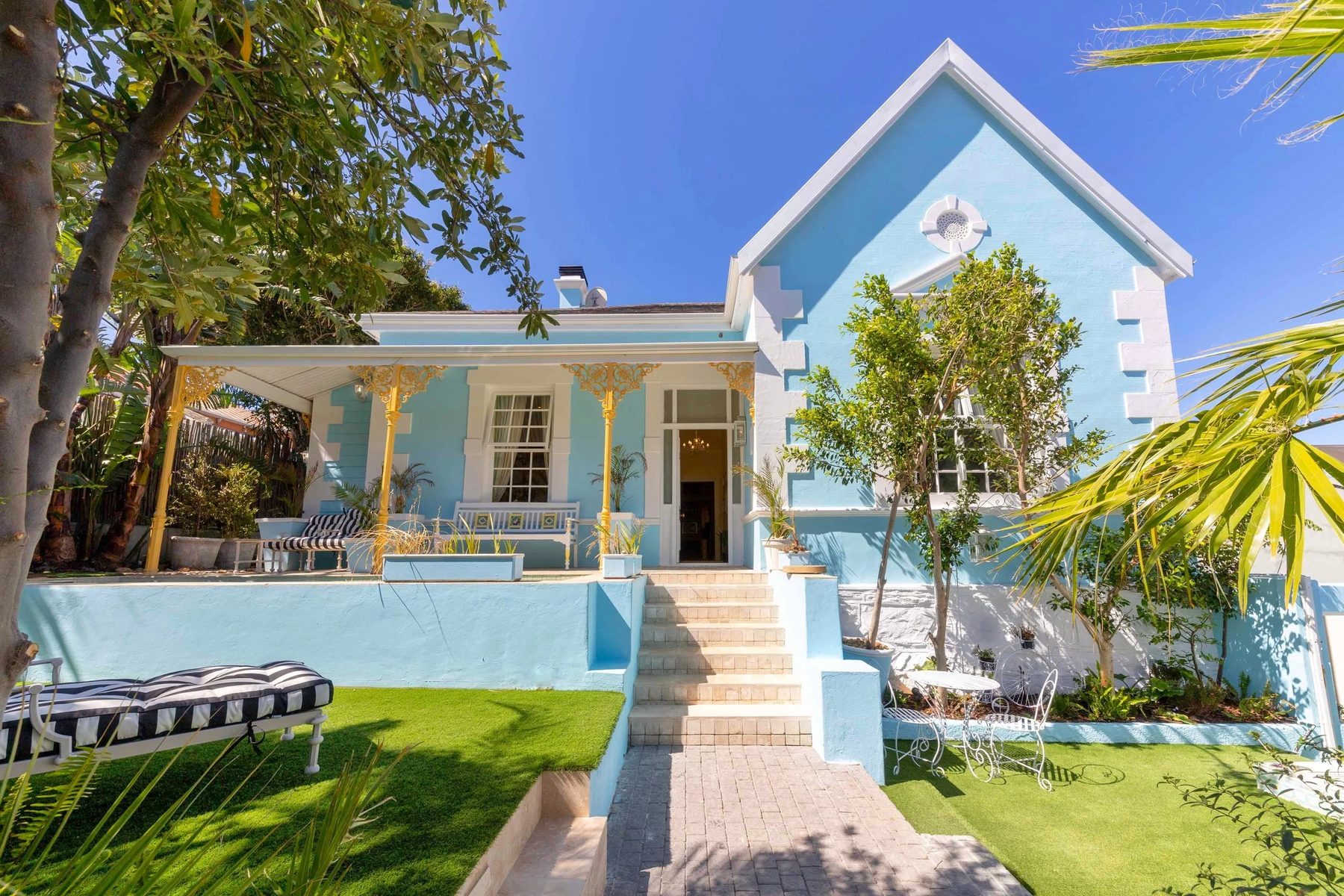 Amina from the garden: the powder-blue gable, the yellow lace verandah, the white steps up from the lawn and the open front door