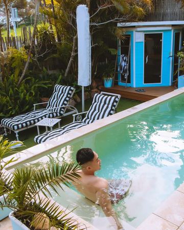 A guest relaxing in the pool, the sauna cabin and the striped loungers behind