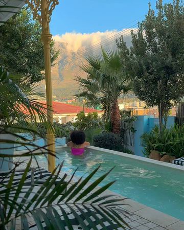 A guest in a pink swimsuit in the pool, Table Mountain under its cloud