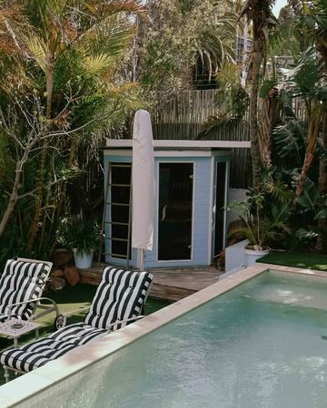 The pool, the striped loungers and the sauna cabin among the palms