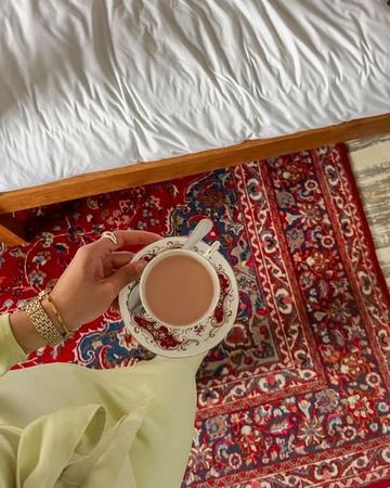 A cup of tea held over the Persian rug beside the bed