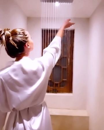 A guest in a robe reaching up to the rain shower