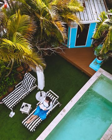 Reading on a striped lounger by the pool, seen from above through the palms