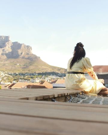 A guest in a cream dress on the deck, facing Table Mountain in the evening light