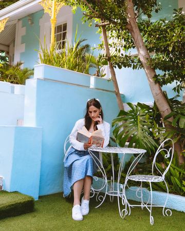 Reading a book at the iron table in the garden by the blue walls