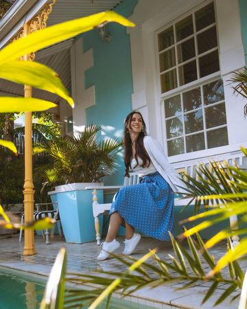 A guest smiling on the white bench beside the pale blue house, palms in front