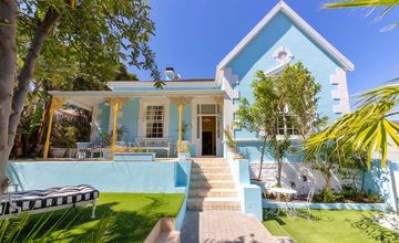The garden front of Amina in the sun: the blue gable, the yellow lace verandah and the steps up from the lawn