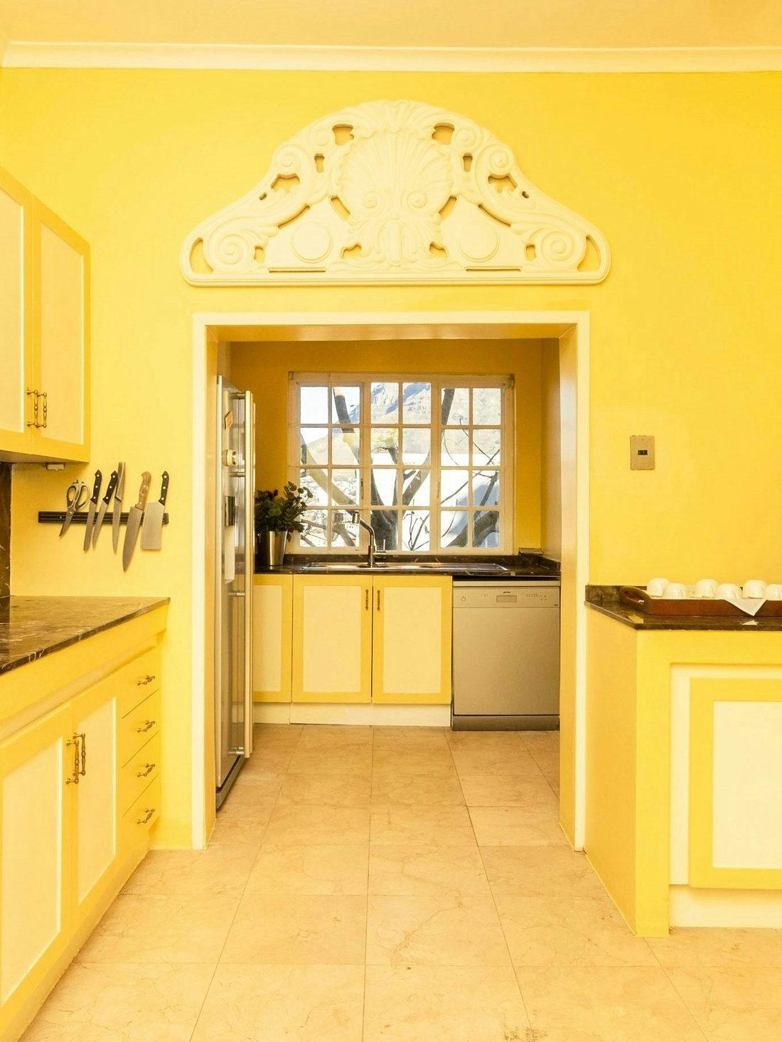 The yellow kitchen, its carved white arch and a window onto the garden