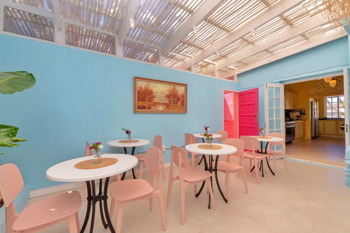 The Morning Palette under its pergola: pink chairs, round white tables and a pink door