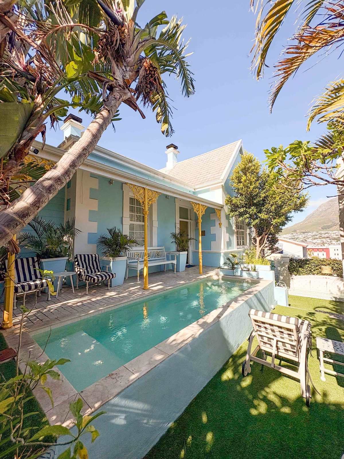 The long pool beside the house, striped loungers on the paving and the yellow lace verandah behind