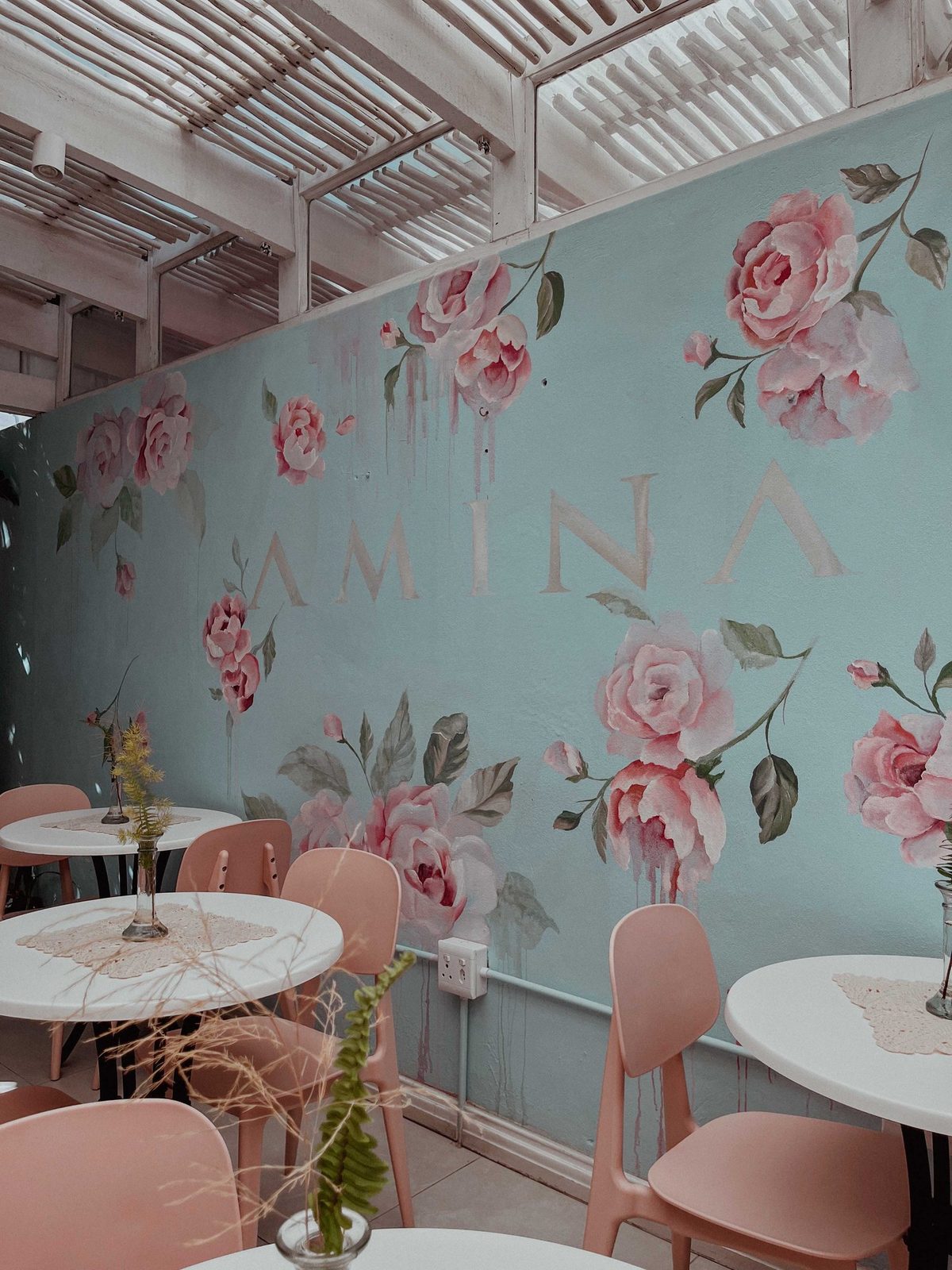 The Morning Palette: pink chairs, round white tables and a mural of pink roses with the word AMINA