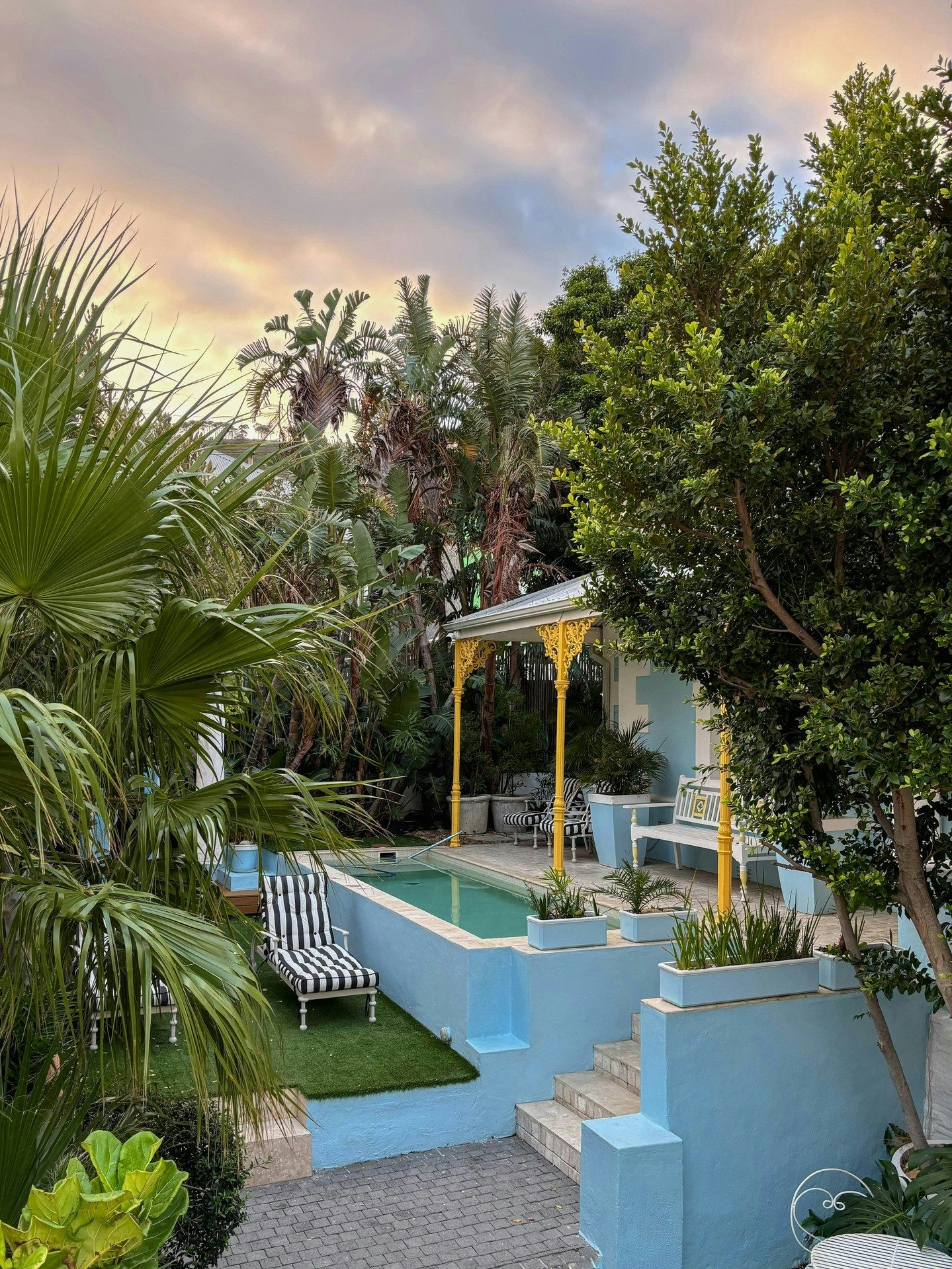 A pastel sunset sky over the pool, the striped lounger and the yellow lace verandah