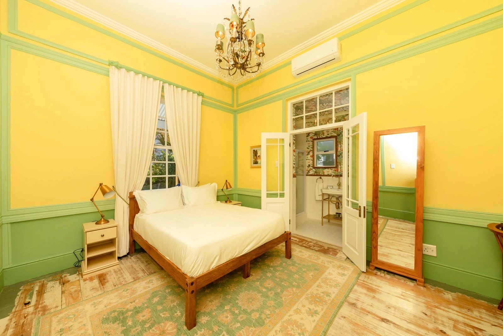 Room 1: yellow walls with green panelling, a chandelier and a queen bed