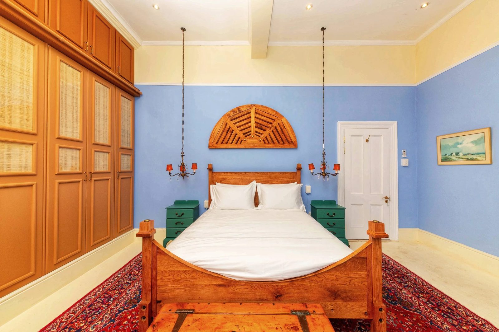 Room 4: blue walls, a carved fan headboard, wooden wardrobes and a red Persian rug