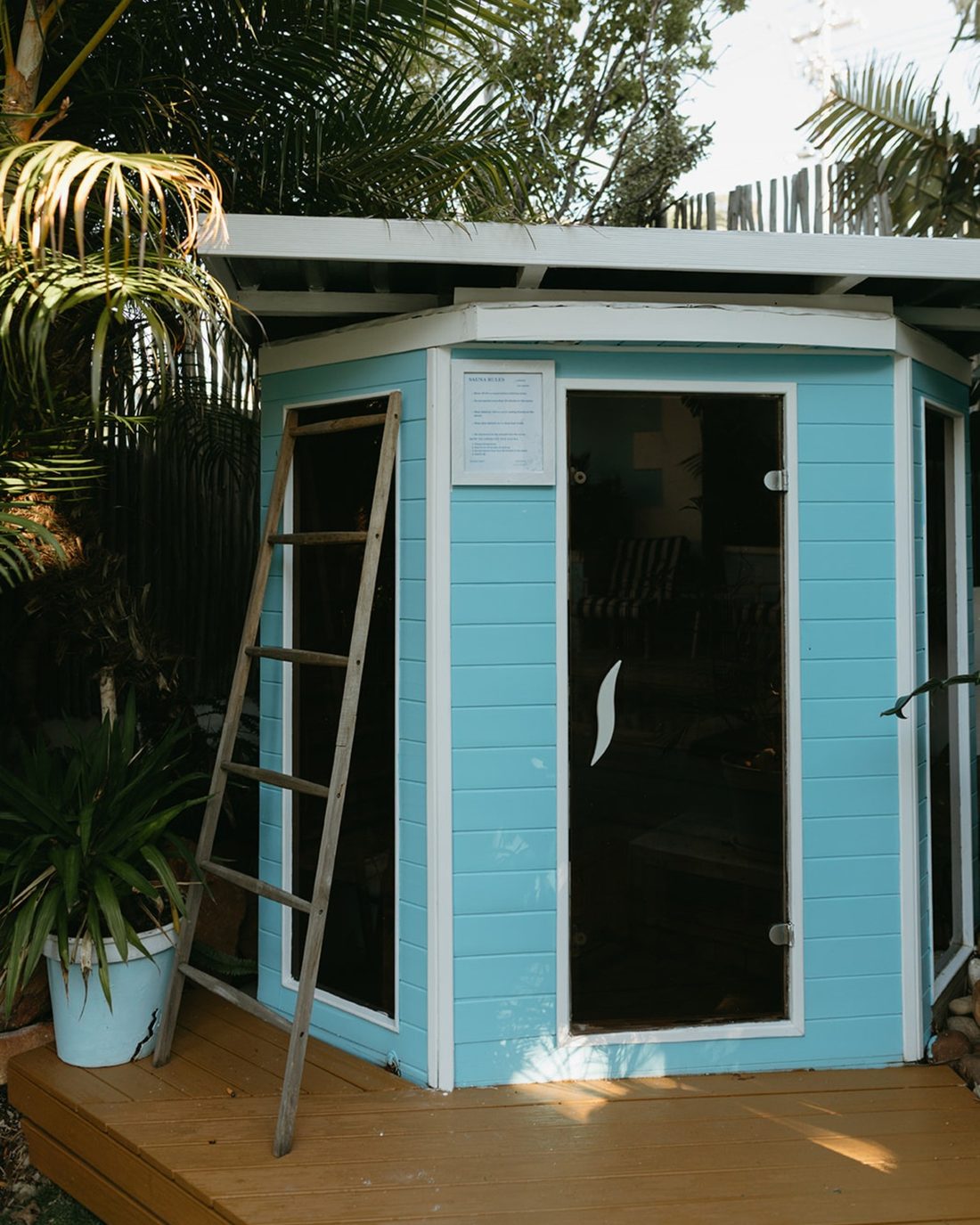 The powder-blue infrared sauna cabin on its wooden deck among the palms